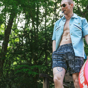 Man wearing sunglasses, blue polo, and black "schooner" mesh lounge shorts and he is holding a lifeguard floatie. 
